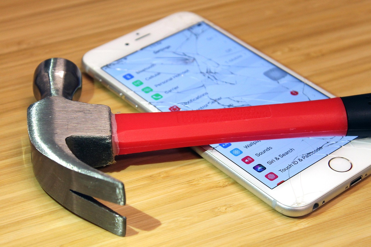 Hammer and Cracked Phone on Wood Desk